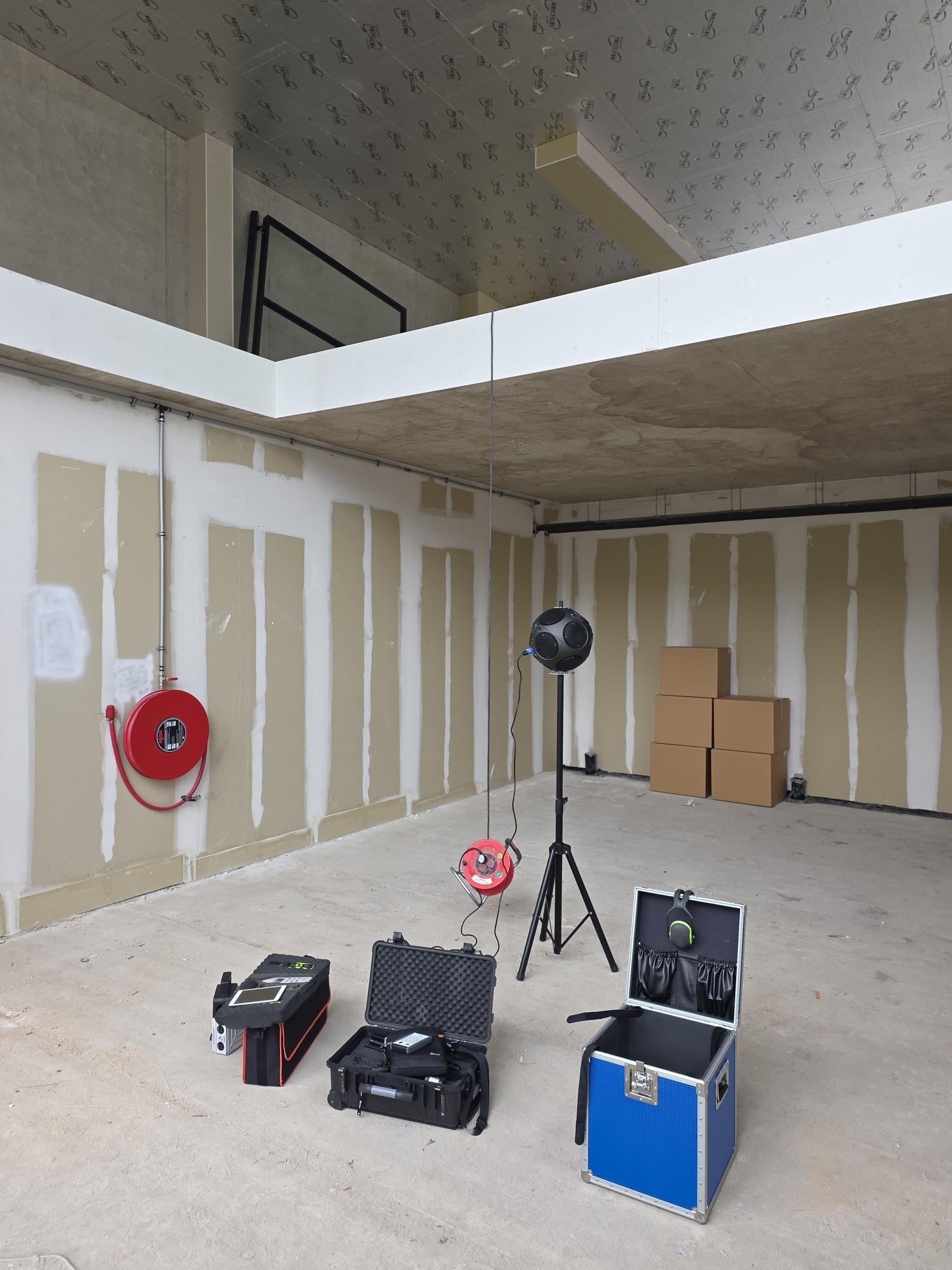 Meetopstelling op een bouwlocatie, met luidspreker op statief en meetkoffers.